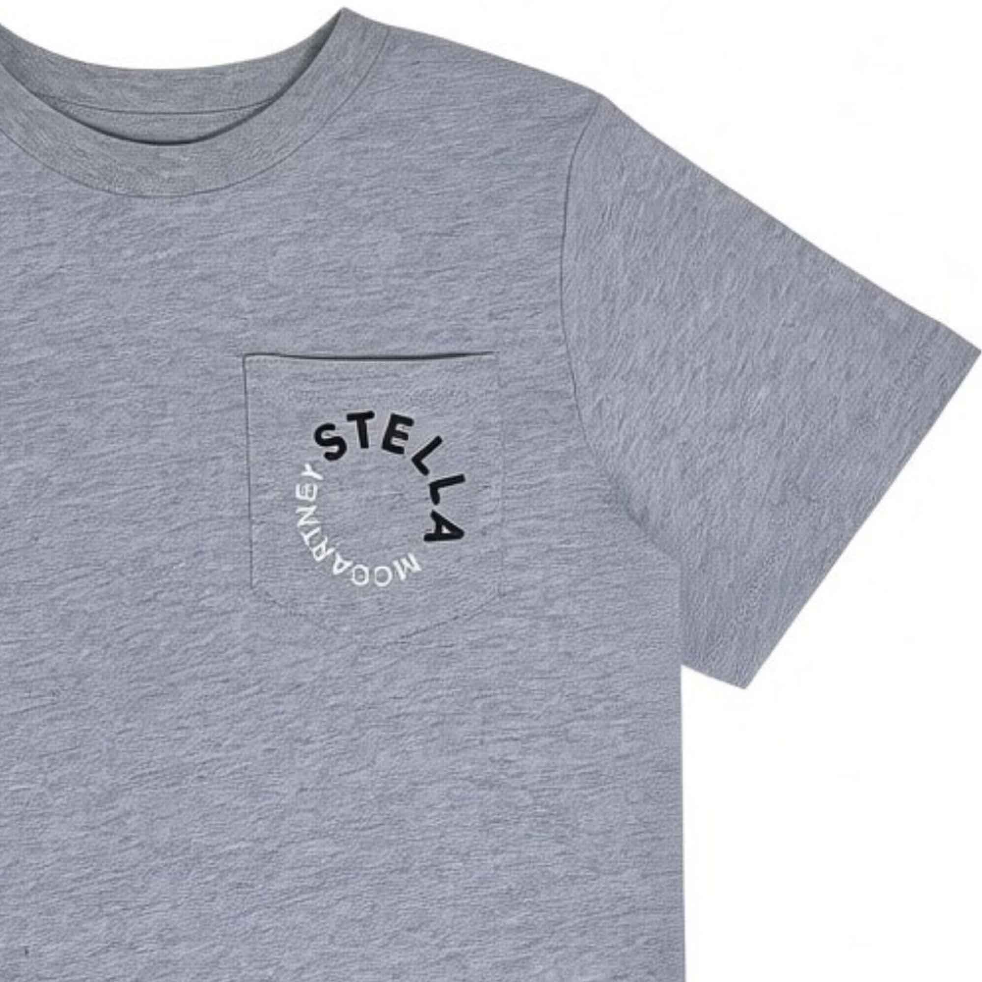 Close-up view of a kids' grey melange T-shirt showing a chest patch pocket printed with a circular "Stella McCartney" logo in black and white.