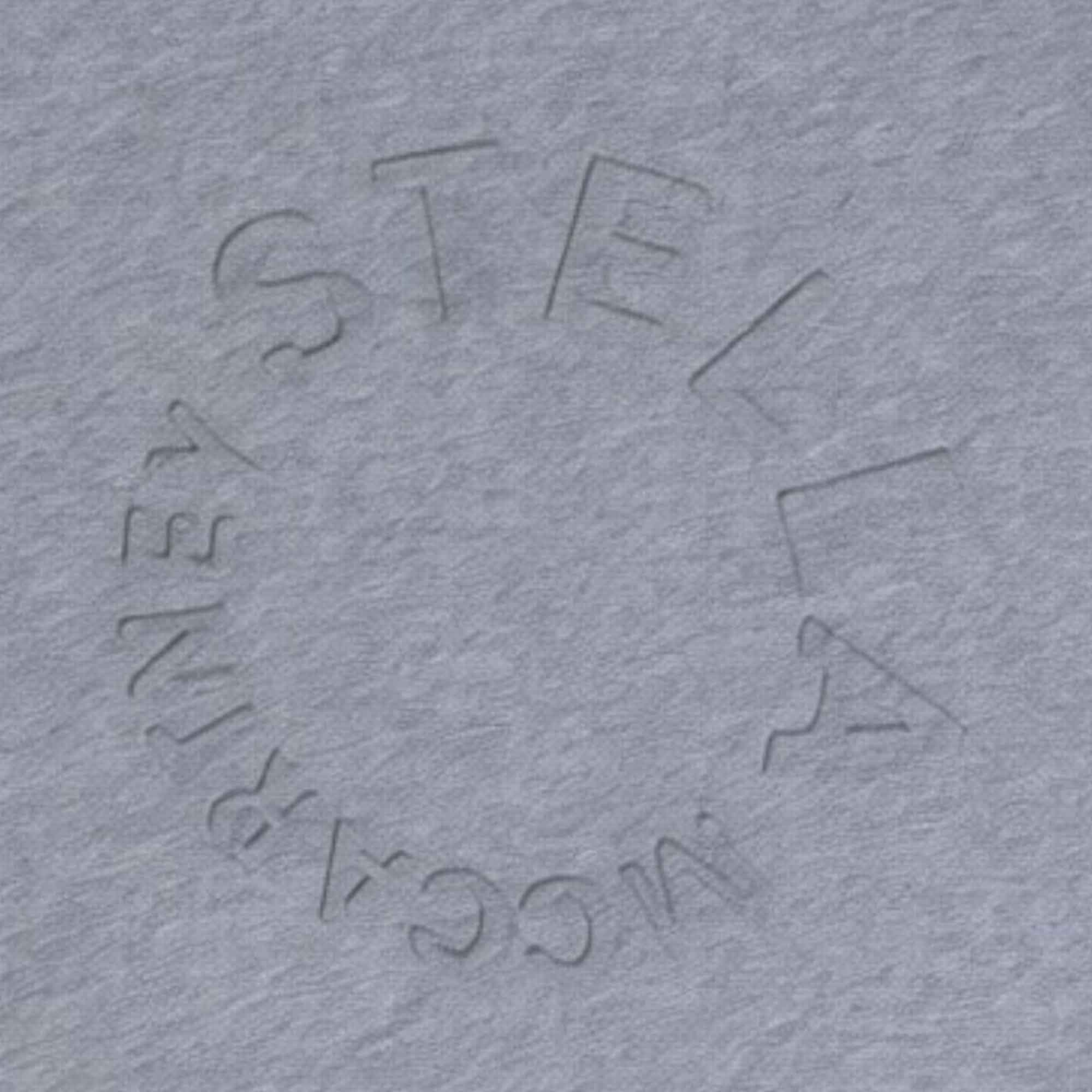 Close-up shot of a grey melange fabric showing the textured, embossed circular logo reading "Stella McCartney".