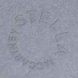Close-up shot of a grey melange fabric showing the textured, embossed circular logo reading "Stella McCartney".