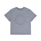 Front view of a kids' short-sleeve grey melange T-shirt featuring an embossed circular Stella McCartney logo on the chest against a white background.
