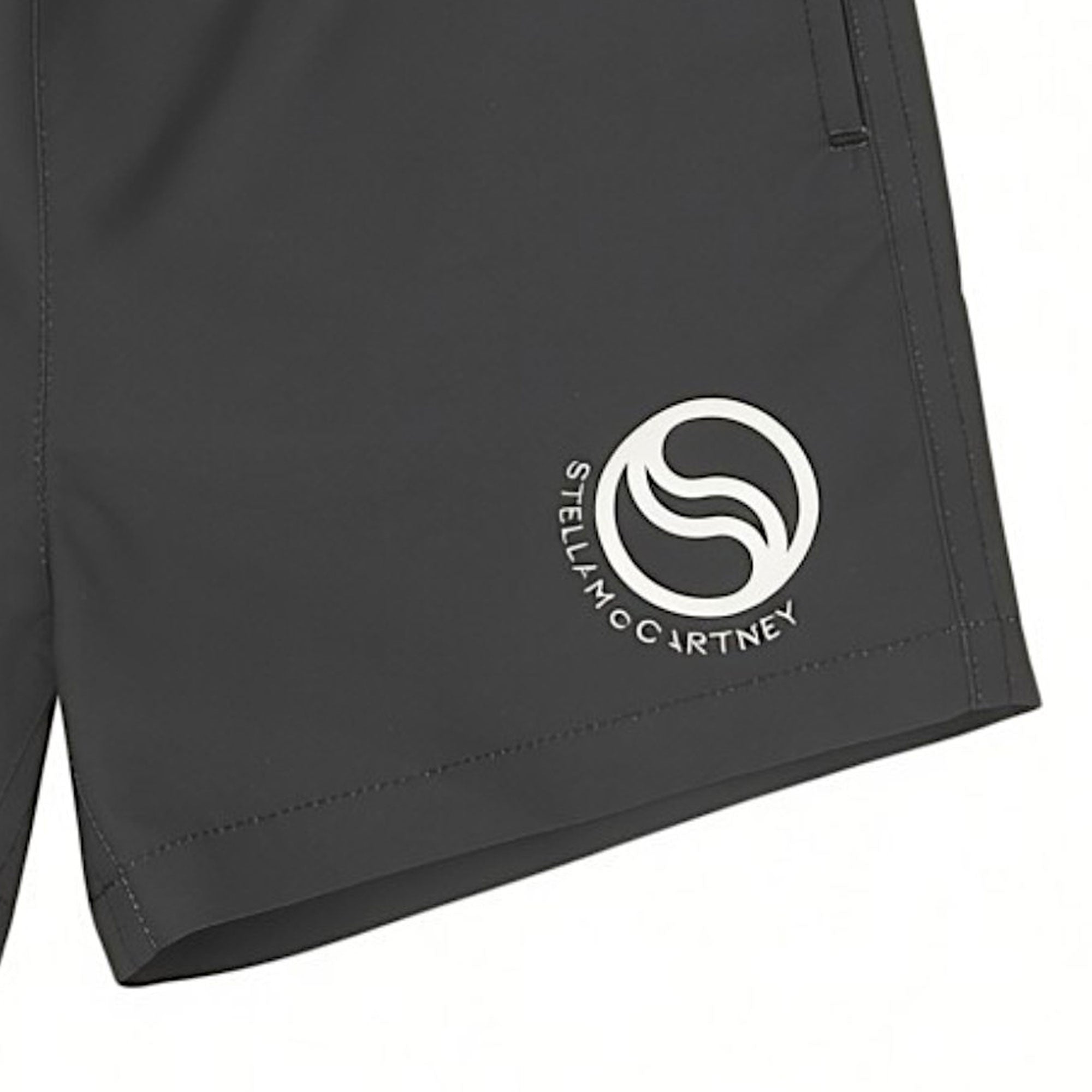 Detailed close-up of the printed white circular S-Wave graphic emblem and brand text on the lower left hem of the dark grey Stella McCartney Kids swim shorts.