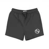 Front view of Stella McCartney Kids swim shorts in dark grey featuring an elasticated drawstring waistband, side pockets, and a white circular logo on the left leg.