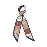 Styled view of the Muni women’s multicolor equestrian printed twilly scarf with horse motifs and teal border. Find the Collection Online