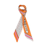 Styled view of the Muni women’s orange printed twilly scarf, with belt buckle motif and brown polka dot detailing. Available for Online Purchase