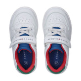 White low-cut sneakers with white laces, blue tongue, red ankle lining, green heel accent, and a Velcro strap.
