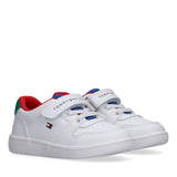 Pair of white Tommy Hilfiger Kids low-cut sneakers with red lining, blue accents, green heel detail, and Velcro straps.