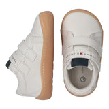 White mid-cut sneakers with tan soles and two velcro straps. Features dark blue accents on heel and tongue, plus Tommy Hilfig
