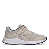 Beige low-cut sneakers with mesh upper, white laces, a velcro strap with "TOMMY HILFIGER" text, and a flag logo. White sole w