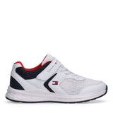 White low-cut sneaker with mesh upper, navy blue accents, red lining, white laces, and a velcro strap. Tommy Hilfiger logo.
