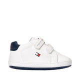 White low-cut Tommy Hilfiger Kids sneaker with navy heel tab and sole, featuring two white Velcro straps and a small flag log