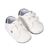 Pair of white low-cut sneakers with navy blue trim, two white velcro straps, and Tommy Hilfiger branding.