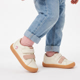 Off-white low-top sneakers with two pink velcro straps, gum soles, and a pink heart logo on the left shoe's side.