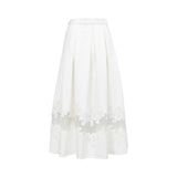 Back view of the Tuba Ergin high-waisted pleated maxi skirt, showcasing its clean lines and a continuous sheer mesh band with white floral lace embroidery wrapping around the lower hemline.
