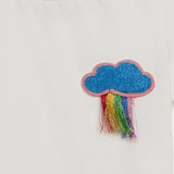 Ivory t-shirt with a blue textured cloud patch outlined in pink, featuring fringed metallic rainbow threads below.