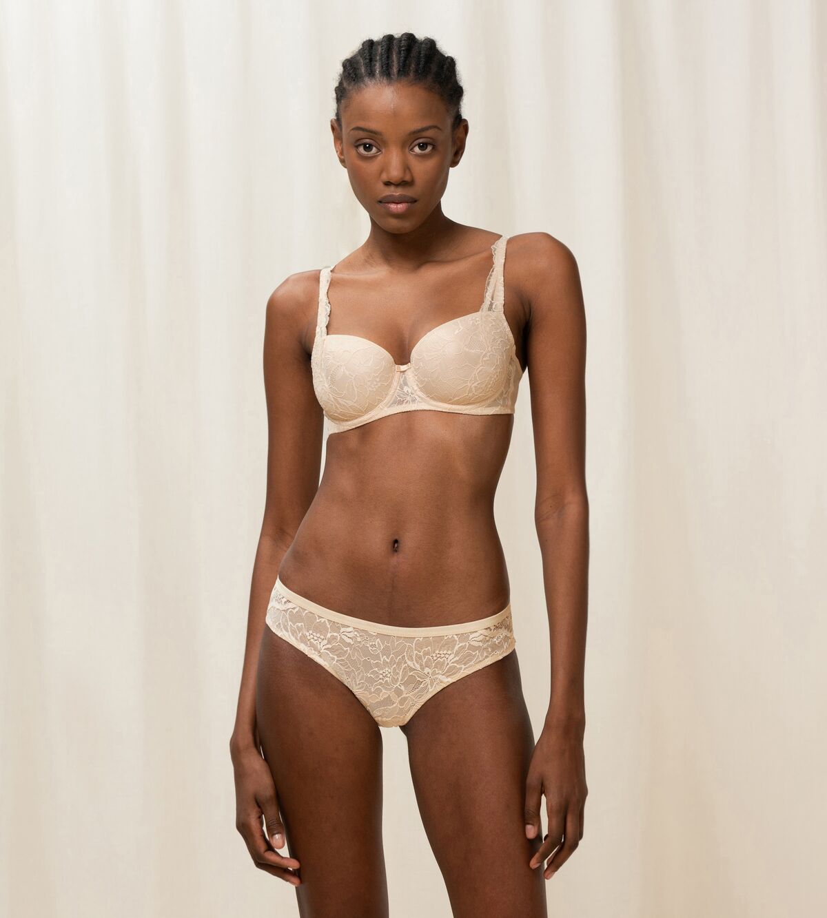 Triumph Amourette Charm Brazilian panties in light beige second model full front view, featuring semi-transparent floral lace and flat edges. Available Now at Blue Salon Qatar