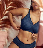 Triumph Amourette Charm non-wired bra in navy blue second front view of model adjusting fit, showcasing the floral design and the intricate lace plunge neckline. Find Now Online