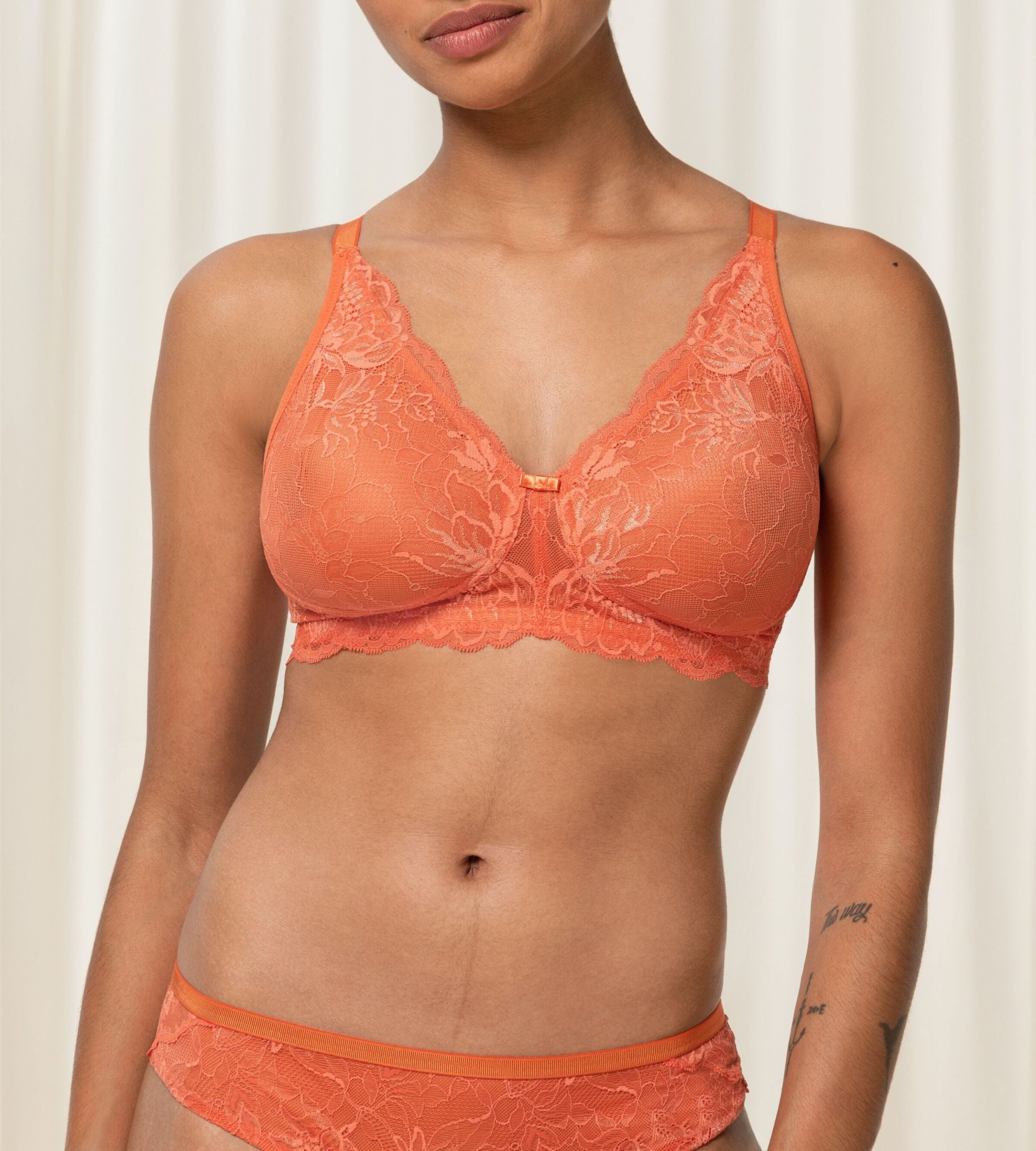Triumph Amourette Charm non-wired bra in orange second model front view, featuring floral stretch lace and a plunging neckline. Shop Online Today