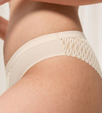 Triumph Aura Spotlight Brazilian panty in light beige model close-up side view, detailing the graphic lace and smooth microfiber. Available Online Today