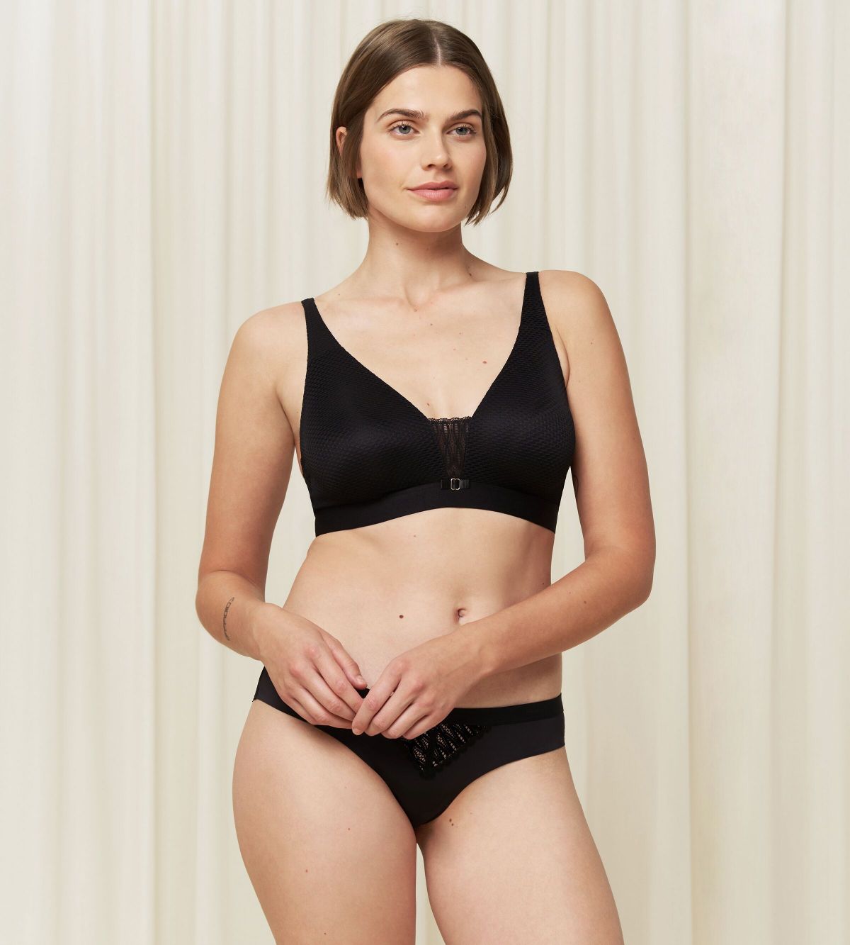 Triumph Aura Spotlight non-wired bra in black third model full front view, showing the plunging lace neckline and comfortable wireless design. Find Now Online
