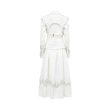 Back view of the Tuba Ergin off-white two-piece ensemble, highlighting a bold open cut-out back on the blazer held by a buckled waist strap, paired with a pleated maxi skirt featuring a sheer lace-embroidered hem.