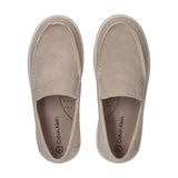 A pair of beige slip-on sneakers with white moccasin stitching, embossed 'ck' logo, and thick white soles. 'Calvin Klein' on