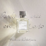 Clear rectangular perfume bottle with light yellow liquid, a white label, and a textured silver-toned cap.