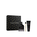 A Valentino Uomo Born In Roma men's gift set featuring a 100ml black rockstud glass fragrance bottle, a 15ml travel spray, and a 75ml tube of shower gel, displayed next to a black gift box embellished with gold stars and the Valentino logo.