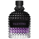 A close-up of a Valentino Uomo Born In Roma Stravaganza fragrance bottle. The glass features the signature rockstud pyramid texture with a gradient transitioning from clear at the base to a vibrant purple in the middle and a deep, translucent black at the top. It is finished with a matte black cap and a black leather-style label with purple branding.