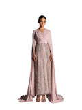 A woman modeling a Velvety brand evening gown in ORCHID ICE featuring a pleated V-neck bodice, a long silver-sequined column skirt, and dramatic floor-length cape sleeves.