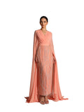 A woman modeling a Velvety brand evening gown in Peach featuring a pleated V-neck bodice, a long silver-sequined column skirt, and dramatic floor-length cape sleeves.