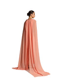 Back view woman modeling a Velvety brand evening gown in Peach featuring a pleated V-neck bodice, a long silver-sequined column skirt, and dramatic floor-length cape sleeves.