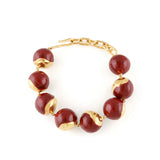 Large orb bracelet with dark red glossy enamel and irregular gold-toned metallic sections, connected by a gold-toned chain an