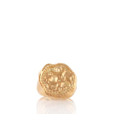 Gold-toned signet ring with an irregular shape and an embossed coin-like motif surrounded by a textured border.