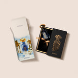dian Granada luxury perfume presentation set featuring the blue bottle resting inside a gold-trimmed black slide box with a palm-shaped cutout, next to an artistic watercolor outer carton depicting Mediterranean architecture and white flowers, from blue salon.