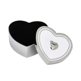 An open silver heart jewelry box revealing a plush black velvet interior, with the decorated white and silver lid resting beside it.