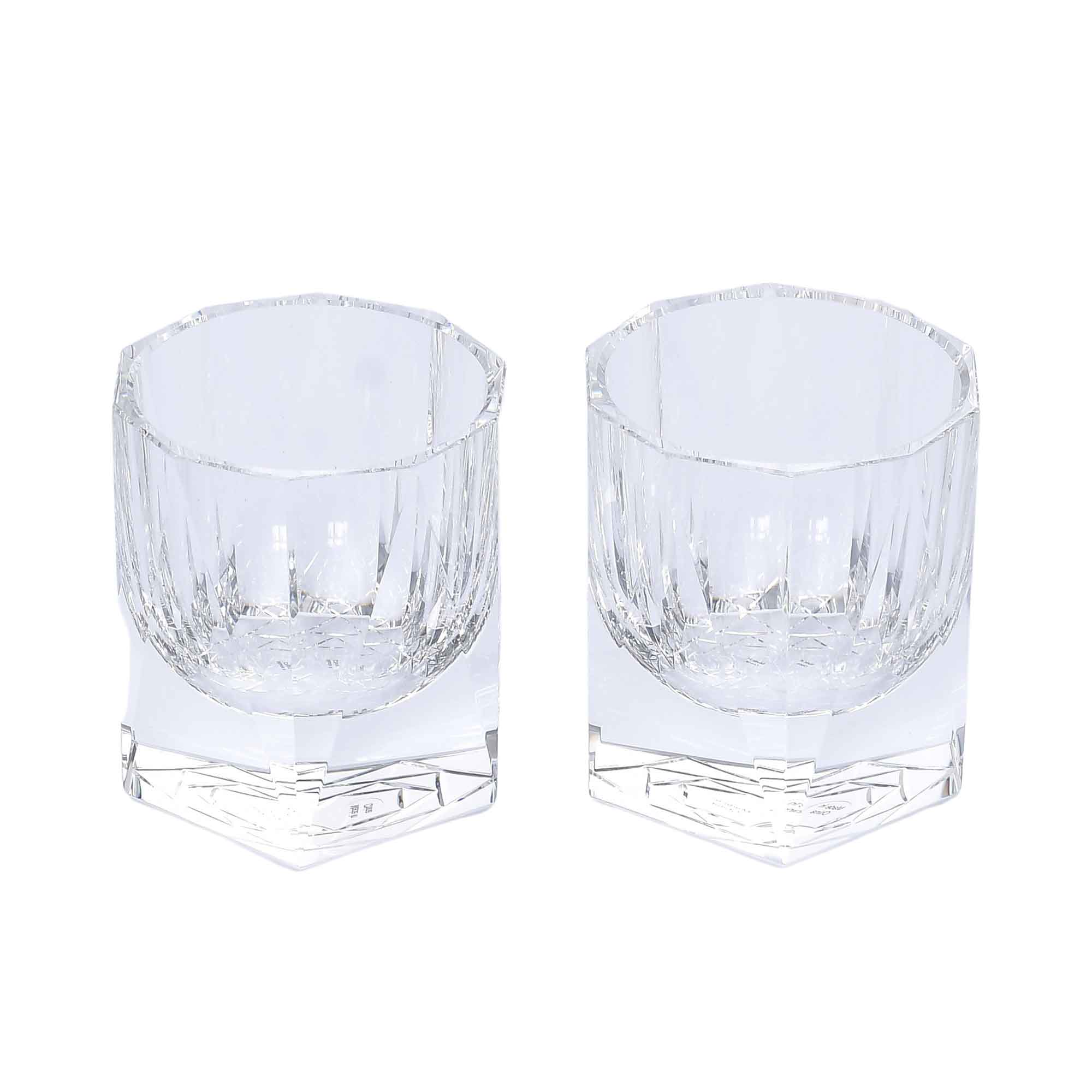 A pair of clear, weighted lowball whiskey glasses with a geometric hexagonal base and vertical light-refracting cuts
