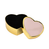 An open heart-shaped gold trinket box showing a protective black velvet interior next to its pink enamel lid.