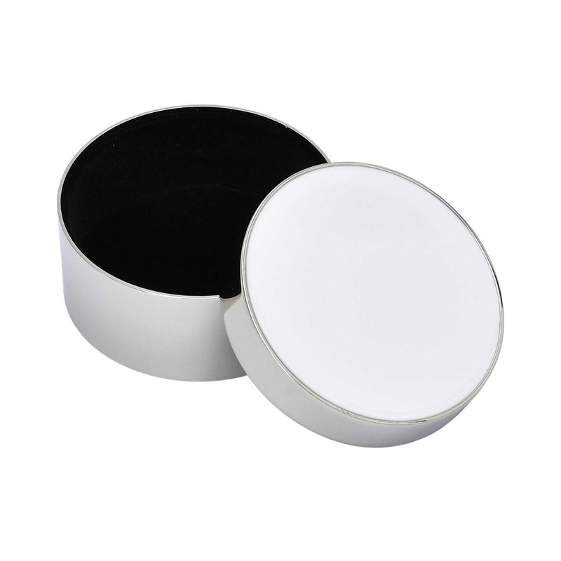 An open cylindrical silver jewelry box displaying a black velvet-lined interior with the white enamel lid resting alongside.