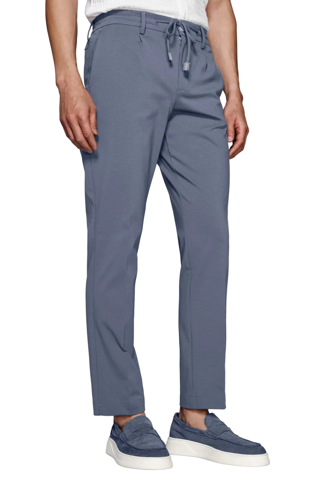Wearing slate blue drawstring trousers with a white t-shirt and blue slip-on sneakers, shown from the waist down against a light gray background.