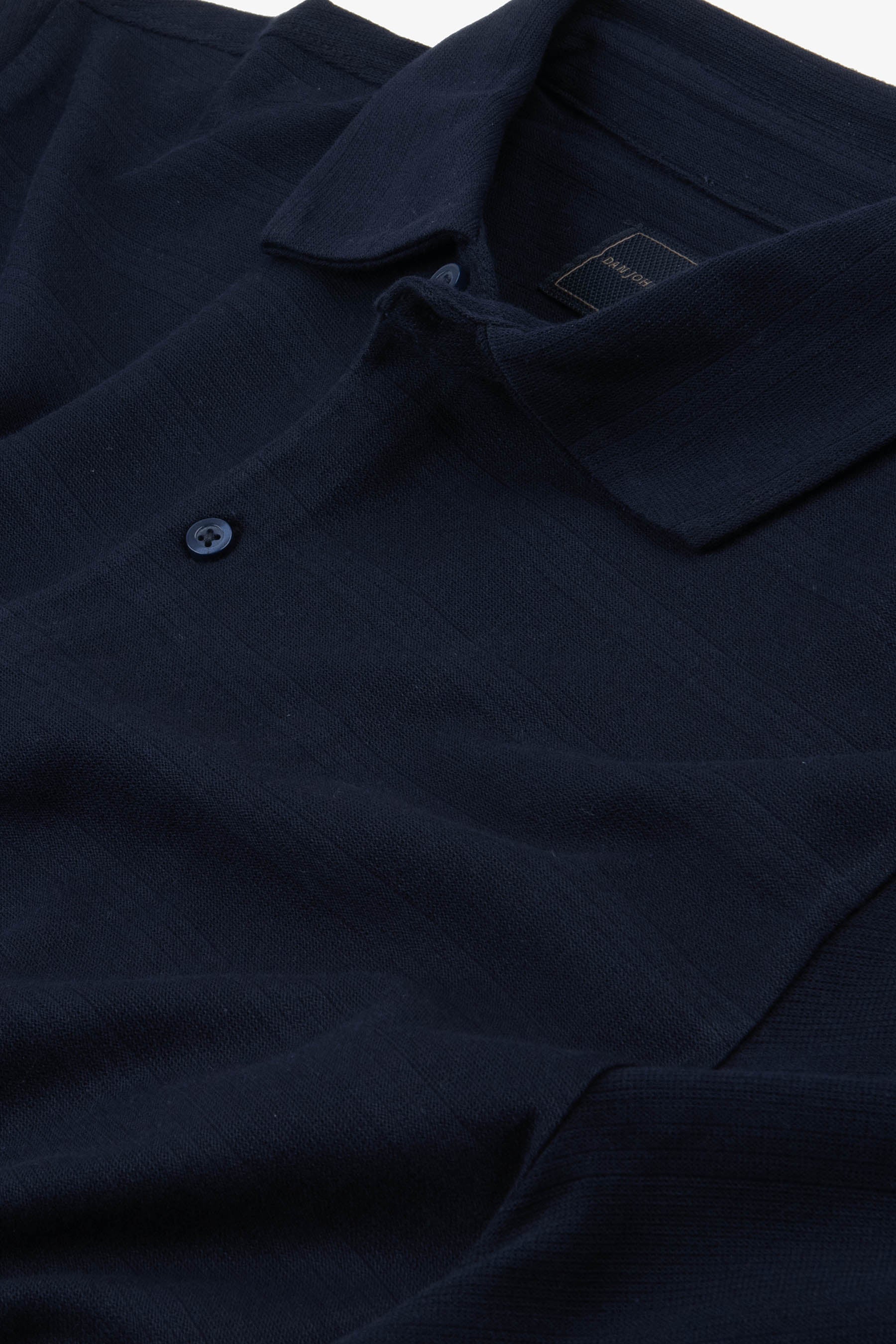 Navy blue textured knit polo shirt with a collar and a two-button placket, featuring a visible dark blue button.