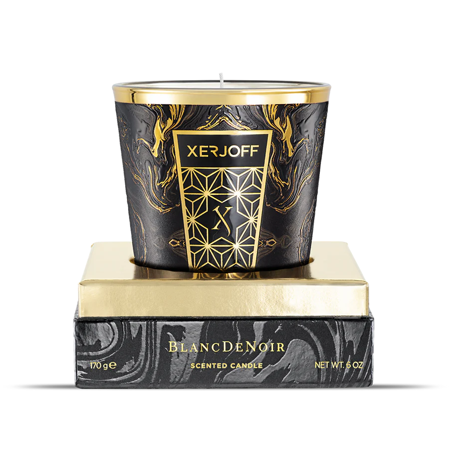 The Blanc De Noir scented candle displayed in an open presentation box, showing the sleek black glass holder decorated with a gold geometric star design and the brand logo.