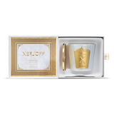 A luxury Xerjoff SilkyGreen scented candle and its gold lid nestled inside a white presentation box with a gold textured frame and satin pull tab.