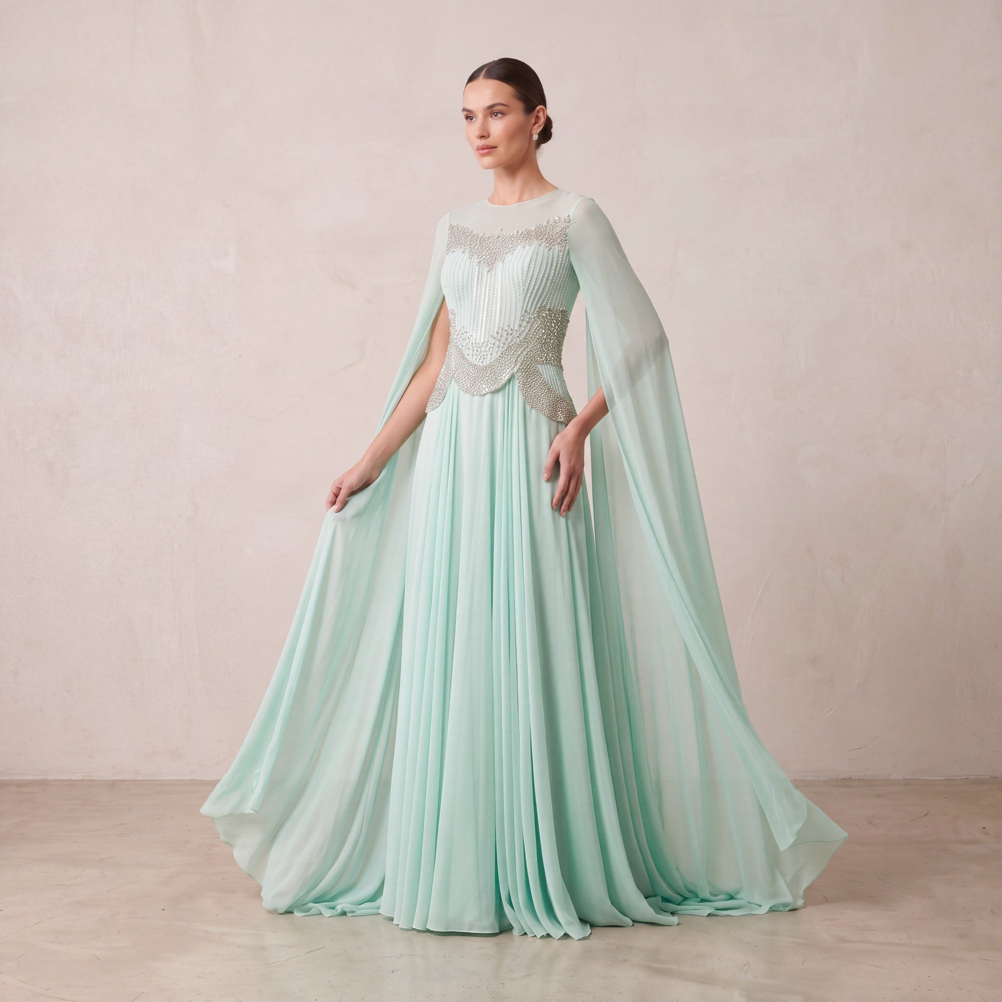 Tiffany blue pleated gown with sheer round neckline, silver-toned beaded bodice, and flowing cape sleeves.