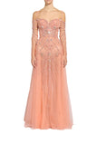 A model wearing a peach pink off-the-shoulder tulle gown with intricate beadwork and embroidery, standing against a light gray studio background.
