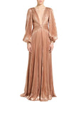 A model wearing a floor-length, metallic rose gold gown with pleated long sleeves, a deep V-neckline, and a gathered waist, photographed against a neutral light gray studio background.
