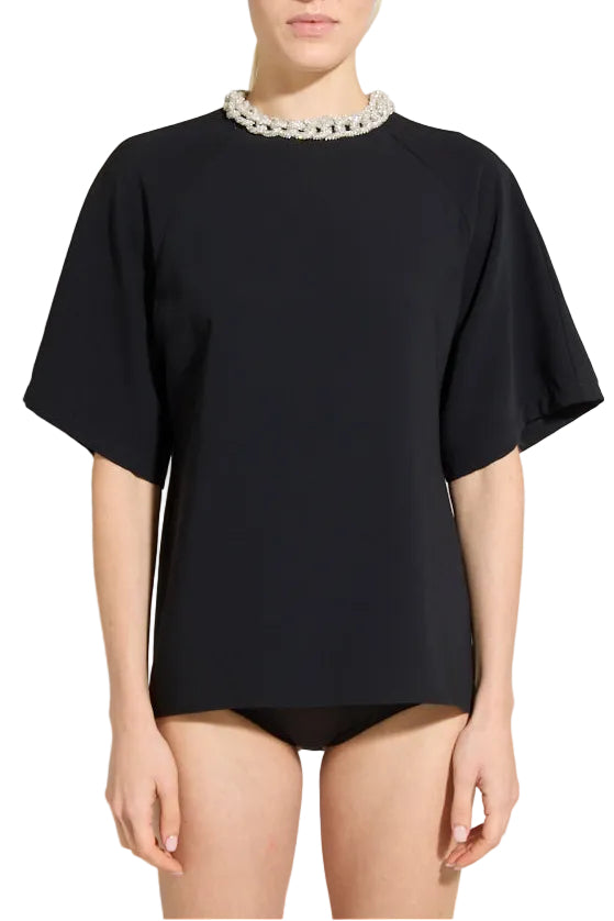 A model wearing a black short-sleeve top with a decorative white beaded collar, paired with black bikini-style bottoms, against a neutral gray studio background.