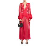 A model wearing a vibrant red sheer mesh maxi dress with long balloon sleeves, a deep V-neckline, and a matching waist belt, holding a small black handbag against a solid white background.