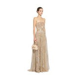 Woman wearing a gold strapless gown holding a matching handbag against a plain background.