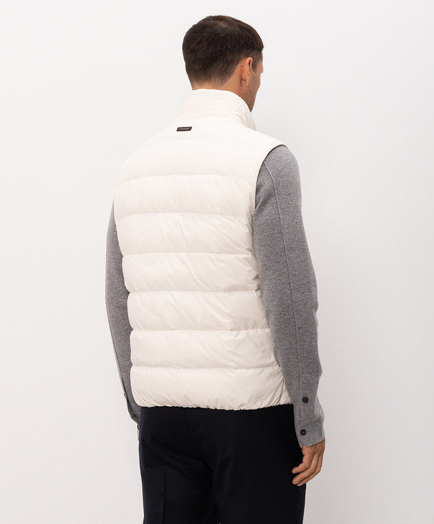 Luminous beige puffer vest with horizontal quilting, a stand-up collar, and a small dark tag on the back collar.