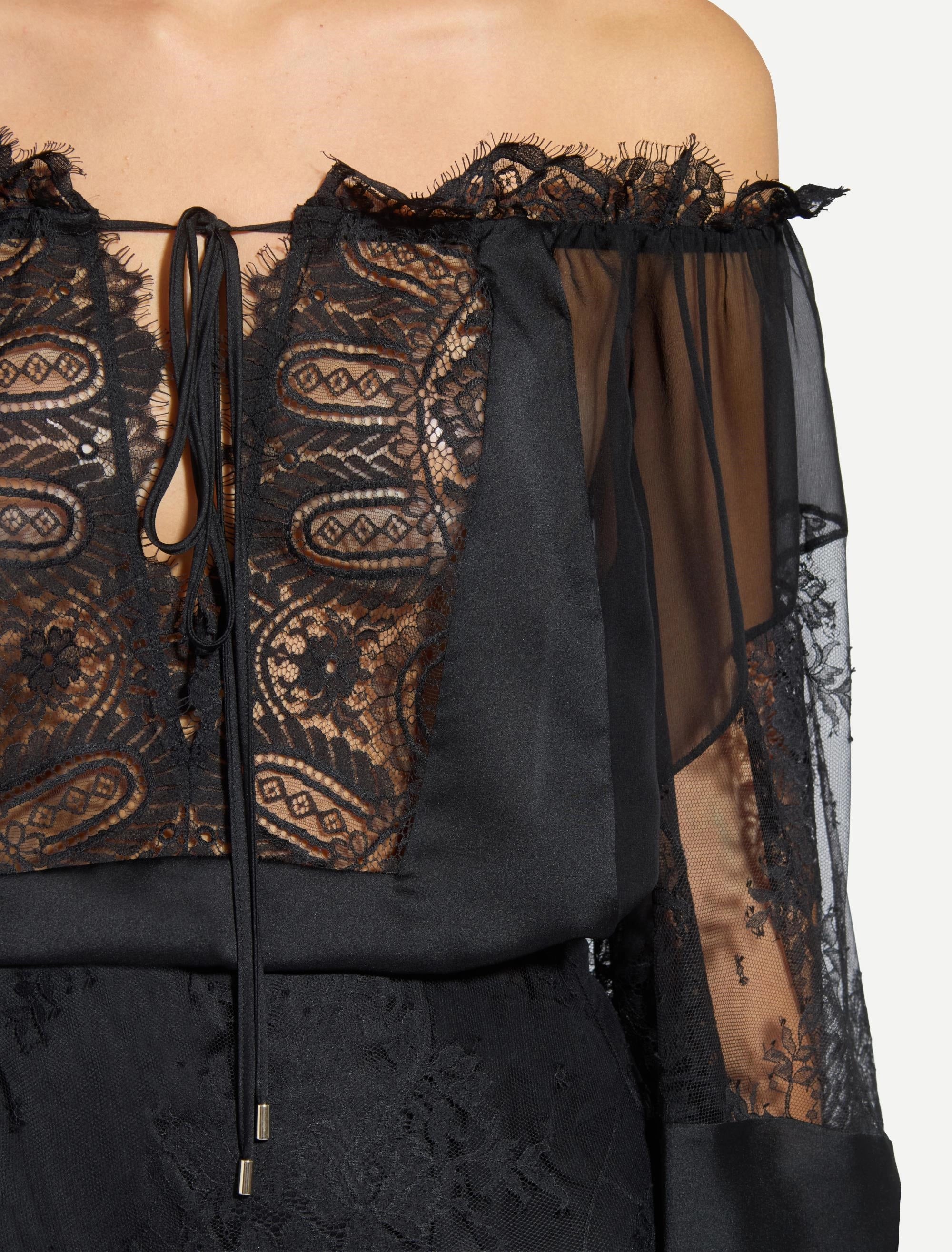 Black off-shoulder blouse with ruffled lace trim, sheer and lace sleeves, and a tie-up V-neck with gold-toned tips. Black lac